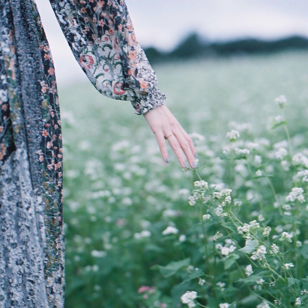 小花柄のワンピースを着て花畑を歩く女性。