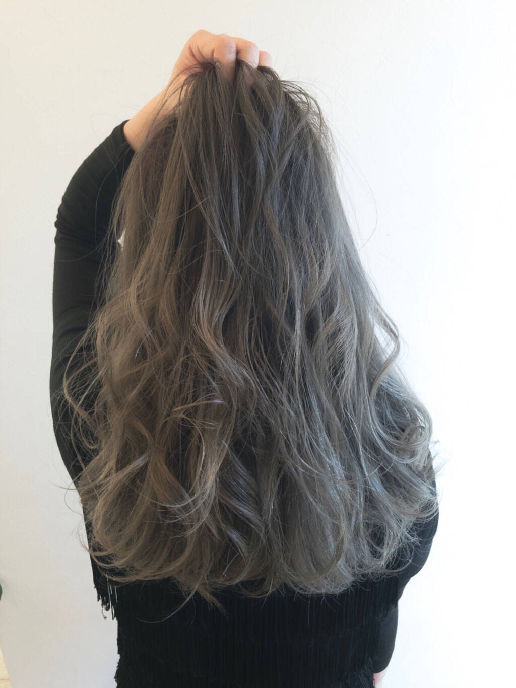 前髪をかきあげるロングヘアの女性の後ろ姿