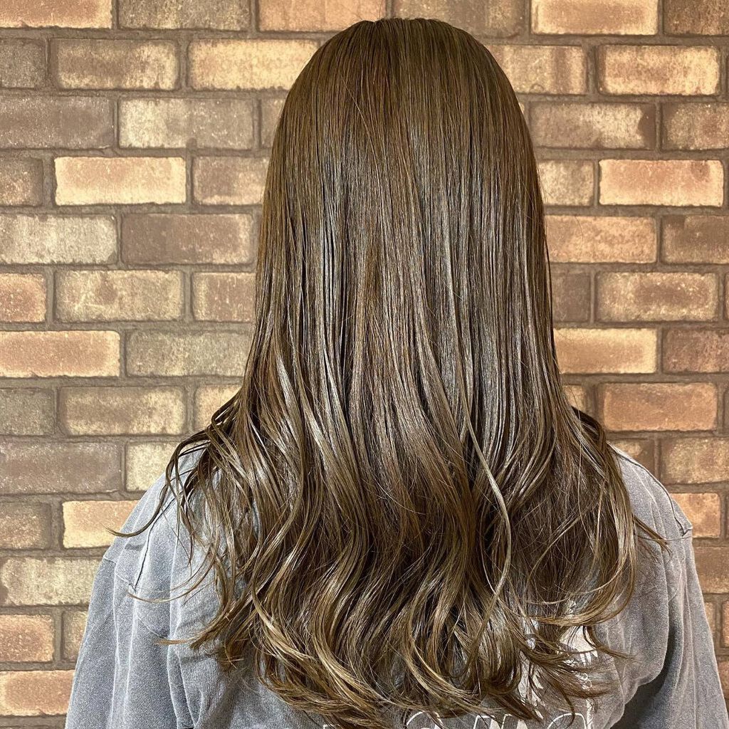 アッシュグリーンカラーの髪色にハイライトを取り入れたロングヘアの女性の後ろ姿