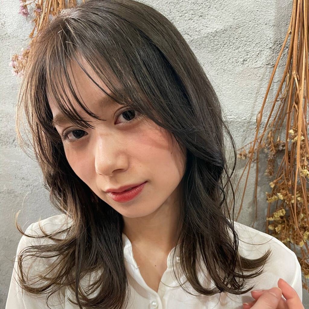 アッシュグリーンの髪色のレイヤーが入ったセミロングヘアの女性