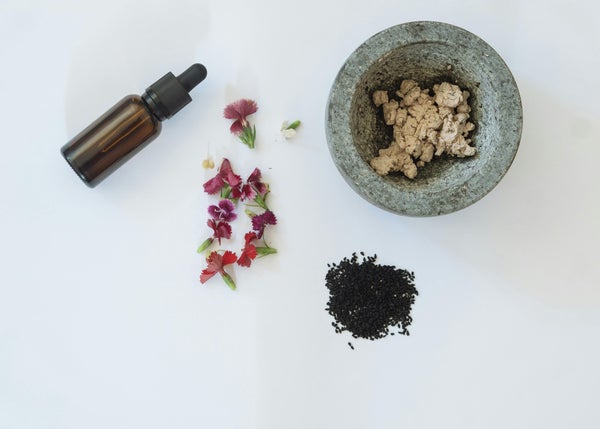 美容液のボトルや花びら・種子・クレイが盛られた器を上から見た様子