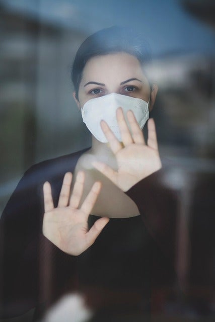 ガラス越しに窓を触るマスクをした女性