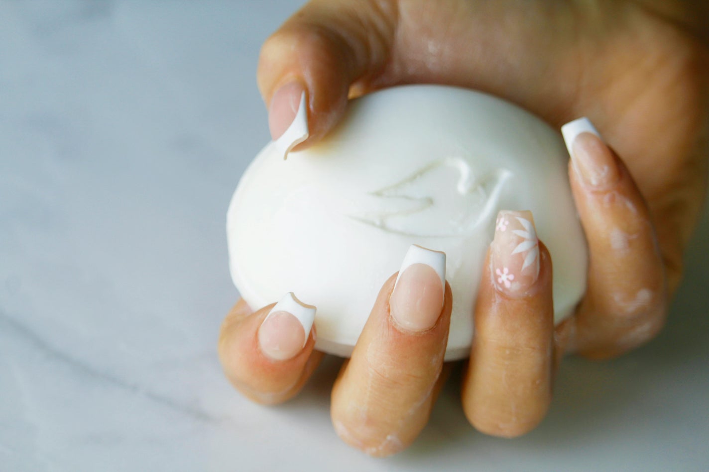 白いスマイルラインのフレンチネイルの指で石鹸を持っている様子