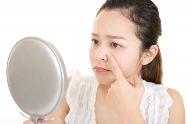 鏡を見ながら小鼻を抑えている女性