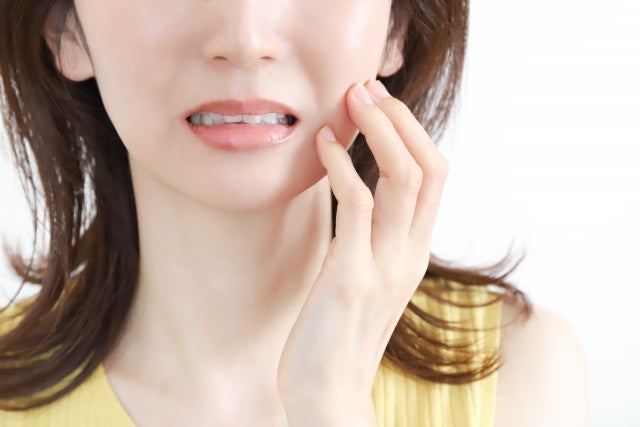 頬のあたりを触っている女性の口元