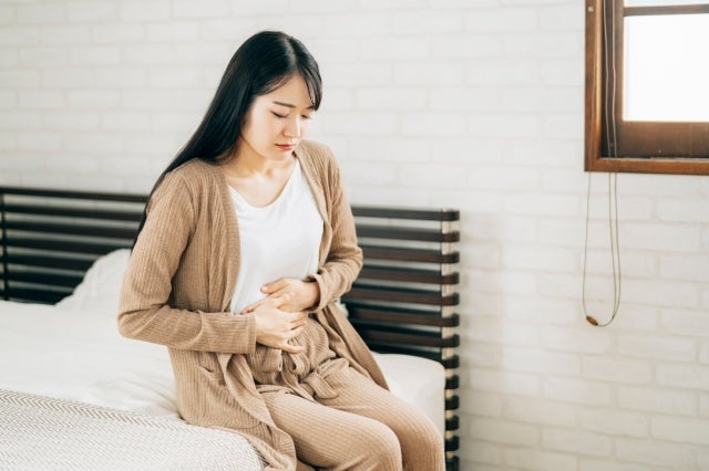 ベッドに腰かけてお腹に手を当てる女性