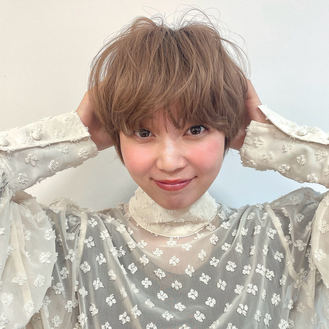 ショートカットの女性が頭に両手を添えている