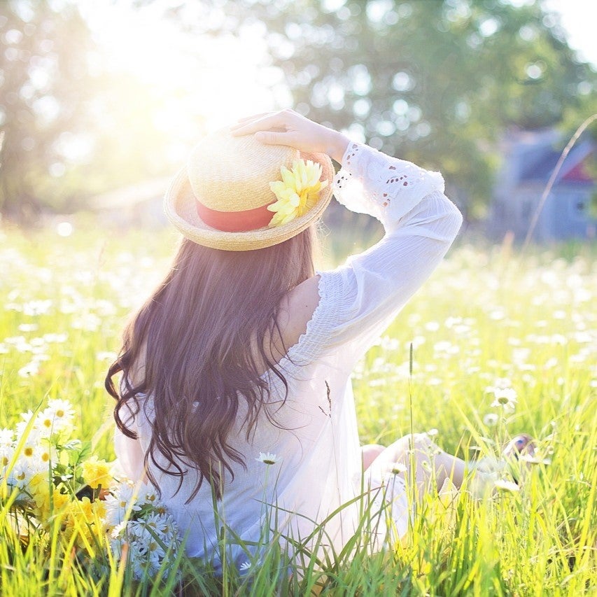 暖かい春の日差しが注ぐ花畑に座る女性の後ろ姿。